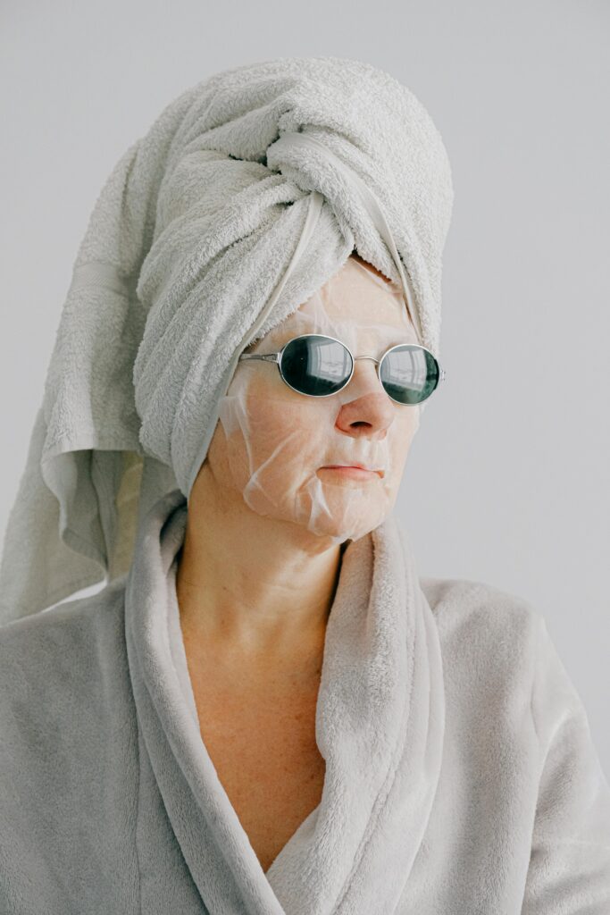Senior woman in bathrobe with face mask and sunglasses enjoying a relaxing moment at home.